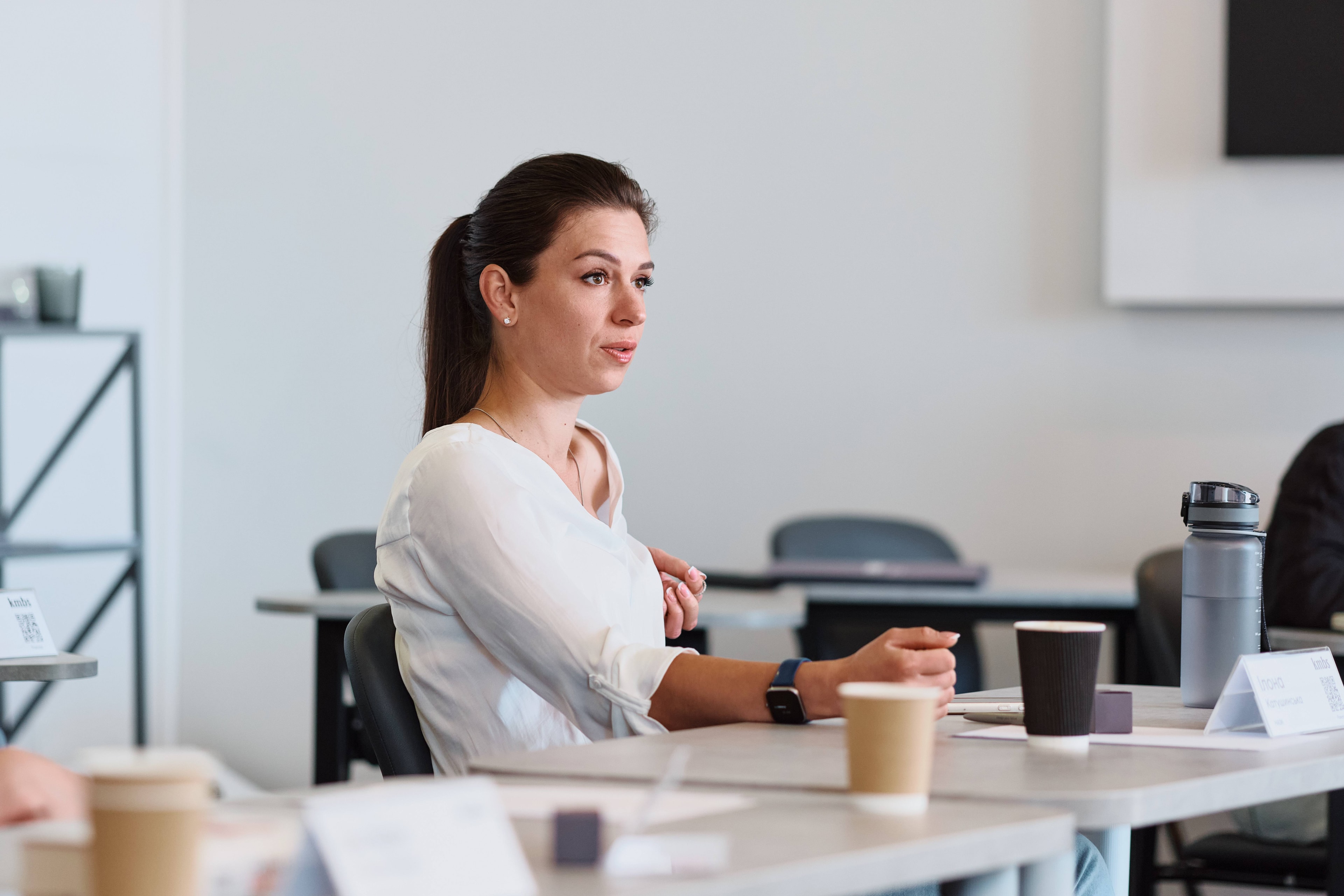 Woman with ponytail seated at a conference table, listening attentively in a bright room.