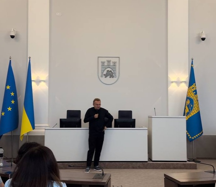 Man speaks at a podium in a formal chamber with Ukrainian and Moldovan flags.