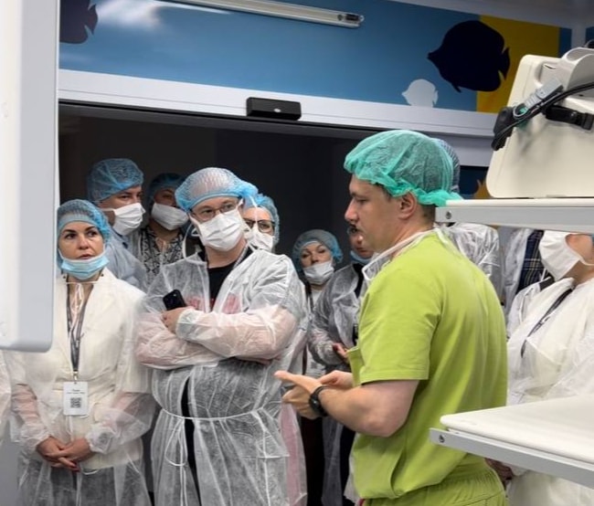 Medical professionals in scrubs and gowns stand in a brightly lit operating room.